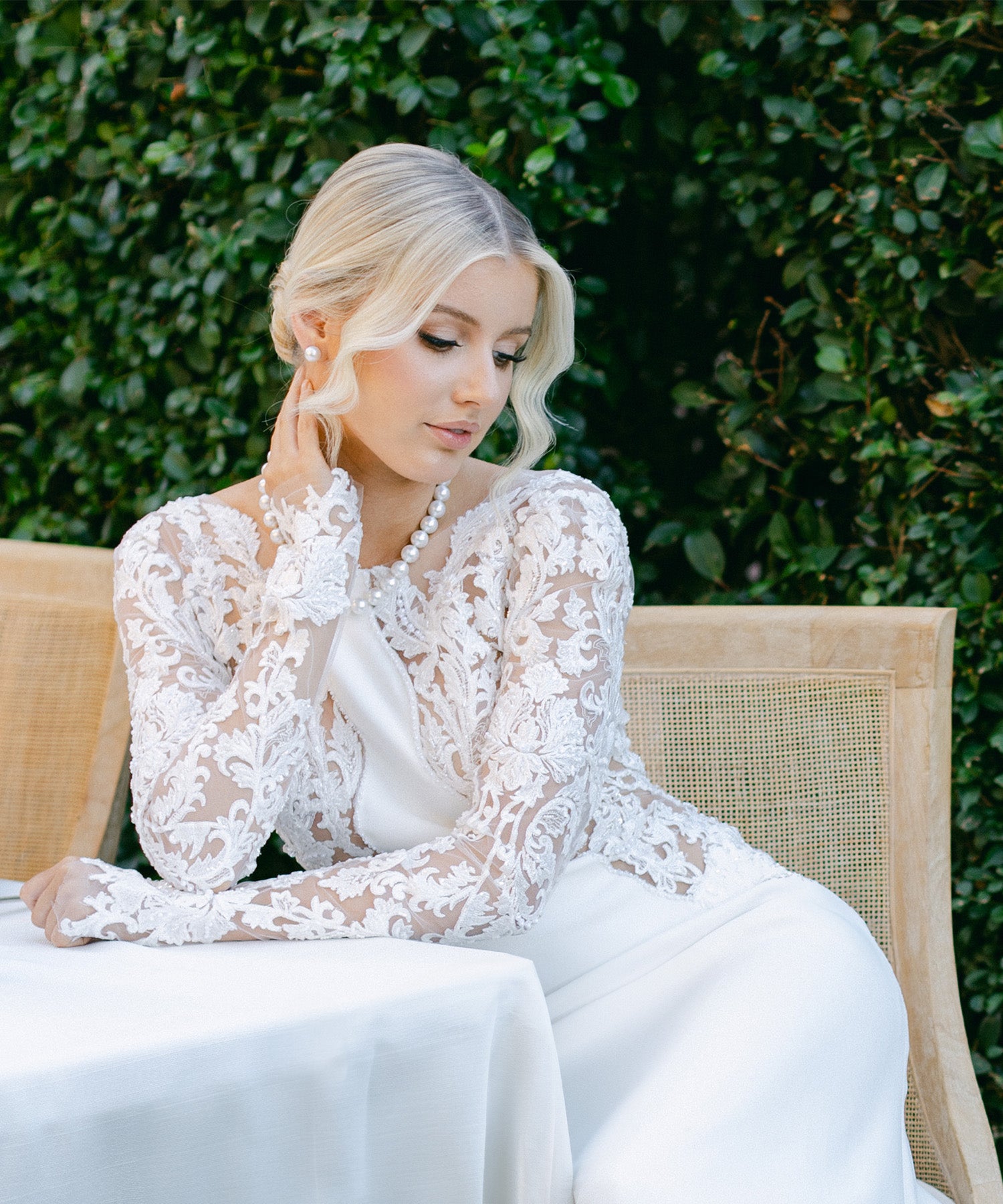 A model in a wedding dress sits elegantly at a table, showcasing the Willie Creek Pearls Bridal Pearl Jewellery Collection, including a pearl necklace and matching earrings.