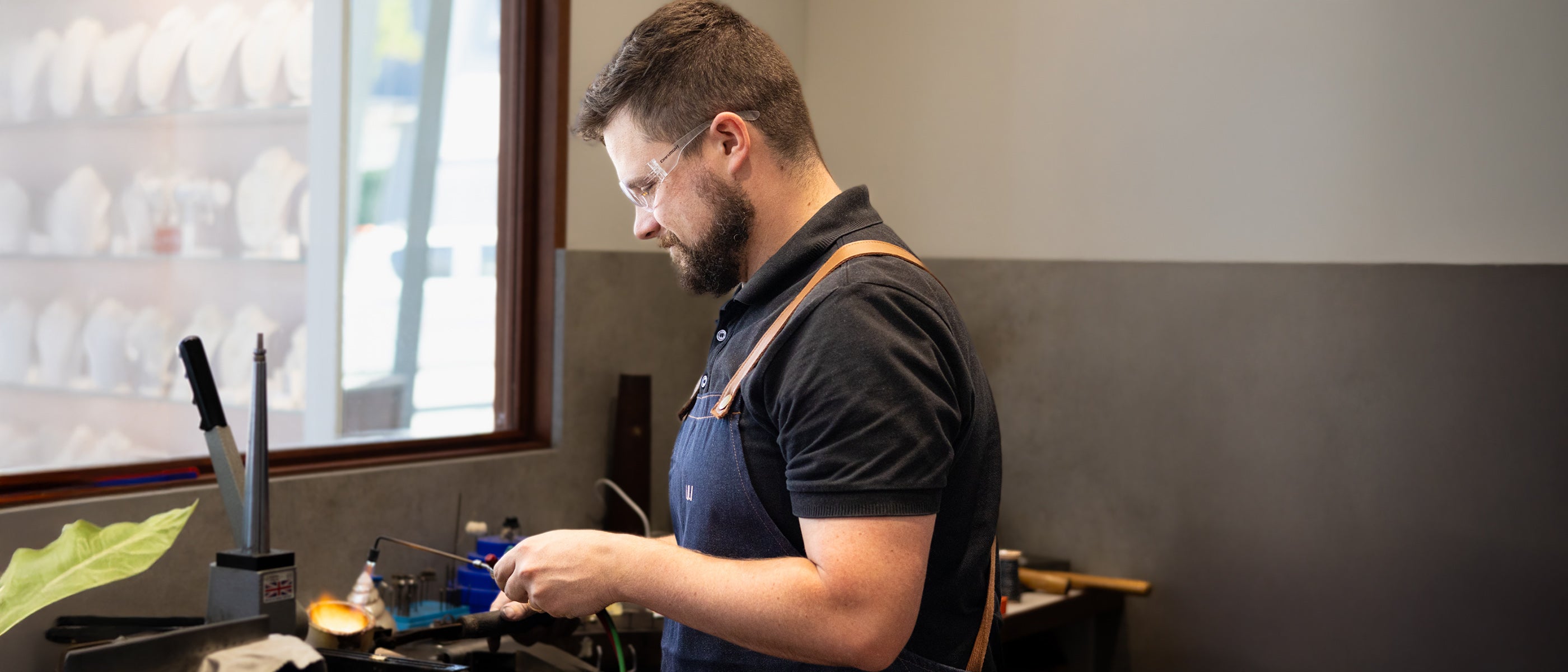 Willie Creek Pearls head jeweller, William, wears an apron and safety goggles while using manufacturing tools to create a new jewellery piece in the Cottesloe workshop.