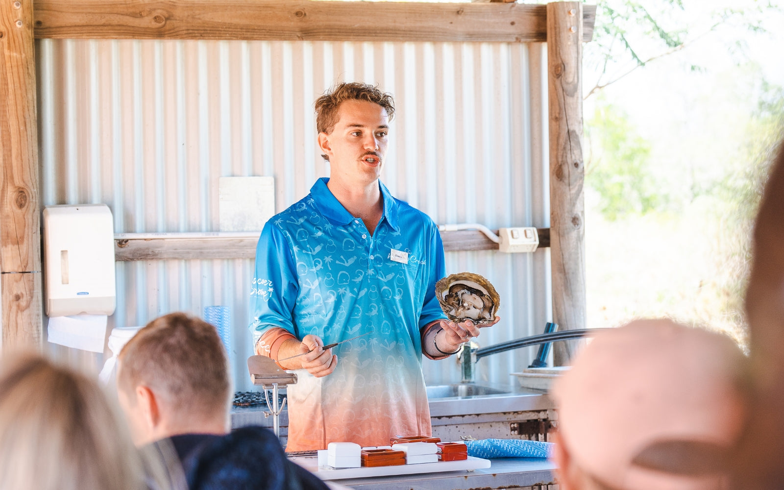 A guide conducting a live pearl harvest on the Willie Creek Pearl Farm tour in Broome, holding an opened oyster shell while speaking to an audience.