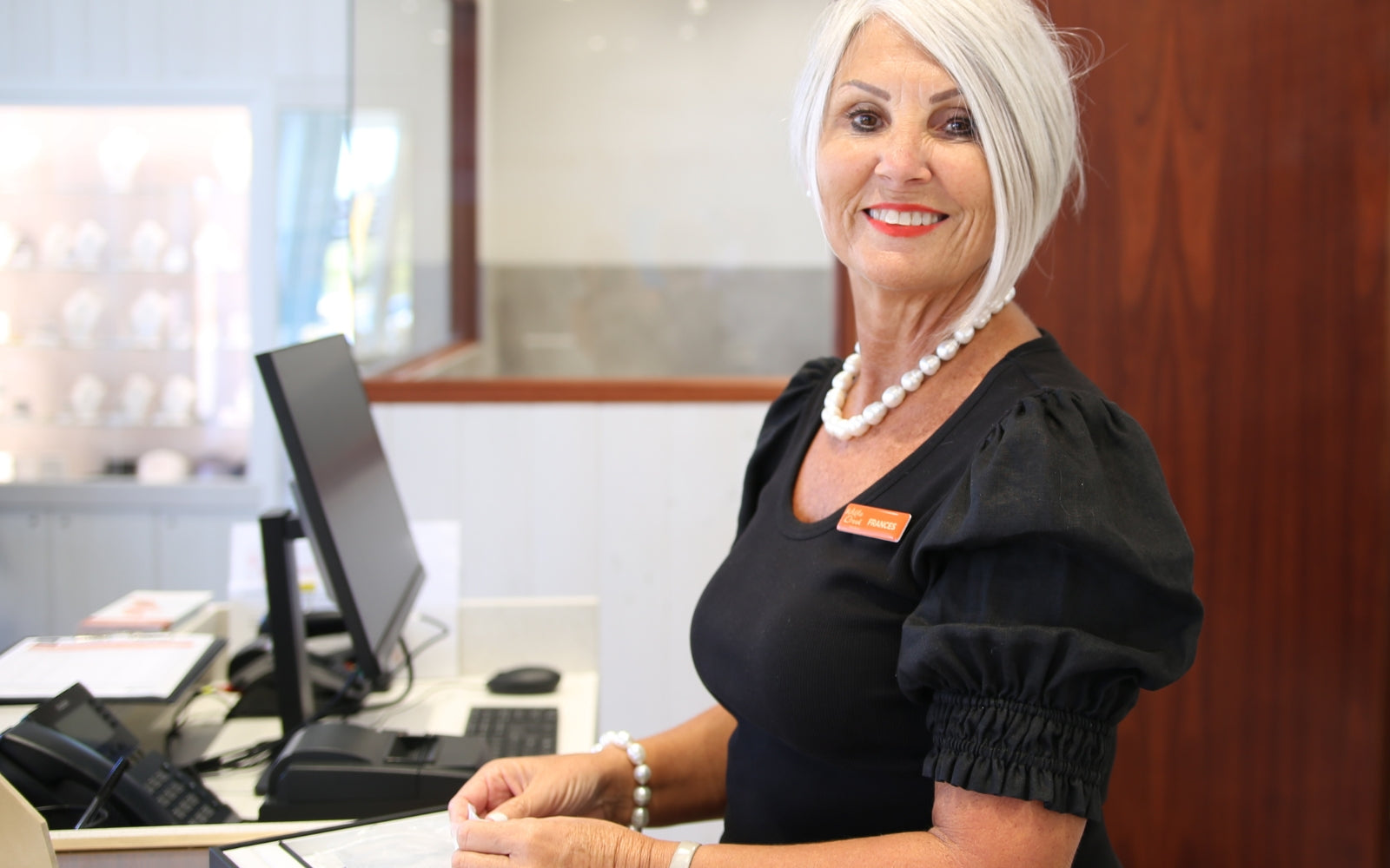 A smiling Willie Creek Pearls Cottesloe showroom team member wears a beautiful pearl bracelet and necklace set while organising pearl jewellery displays at her sales counter.