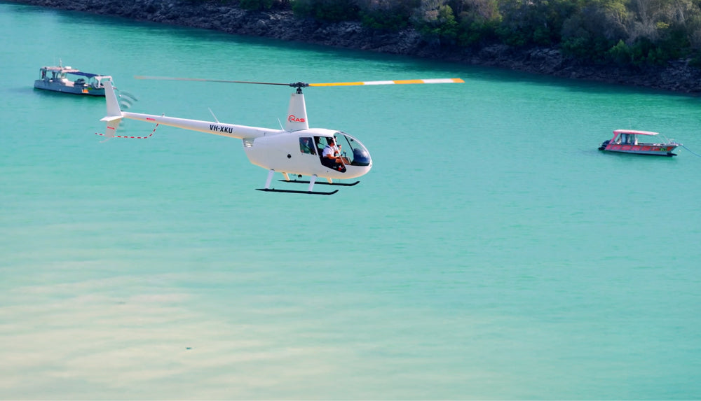 A white helicopter hovers over two boats in the turquoise blue waters of Willie Creek by the Willie Creek Pearl Farm in Broome